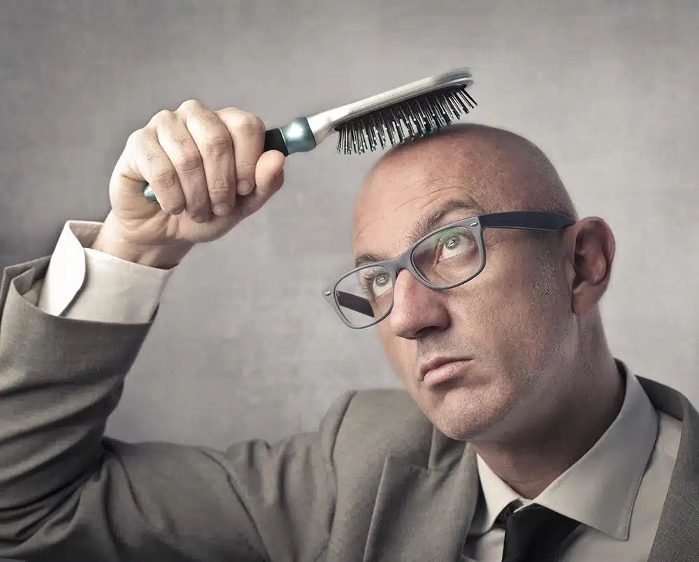 A bald man brushing his head with a hairbrush.