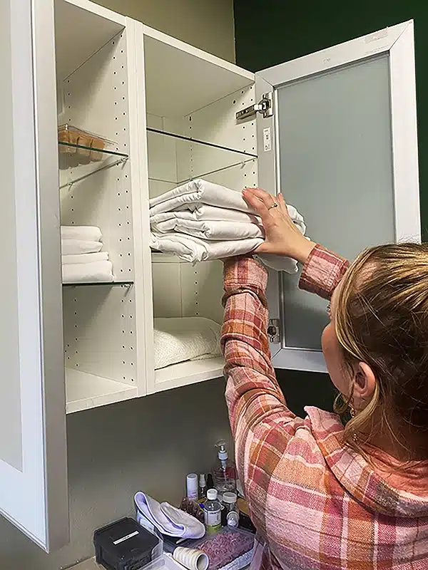 Bello Salon Suites attendant stocking a cabinet with fresh linens.