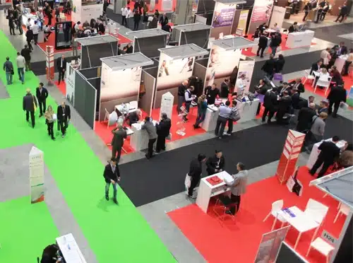 A trade show floor showing display booths and show attendees milling around.